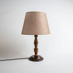 a wooden table lamp with a beige shade on it's base and a black cord