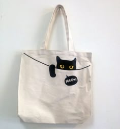 a white tote bag with a black cat drawn on the front and yellow eyes