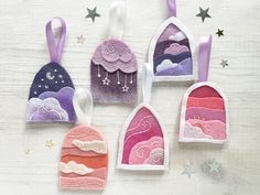 four felt ornaments hanging from strings on a white surface with stars and clouds in the background