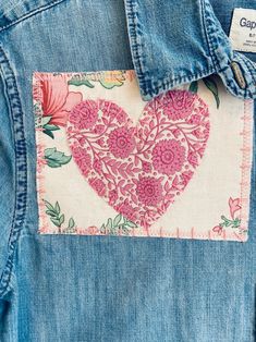 the back of a jean jacket with a pink heart patch on it's chest