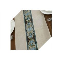 the table runner is decorated with blue and green flowers on beige linen, along with silverware