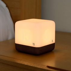 a wooden block sitting on top of a bed next to a night stand with lights