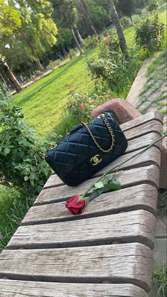 a black purse sitting on top of a wooden bench next to a rose and chain