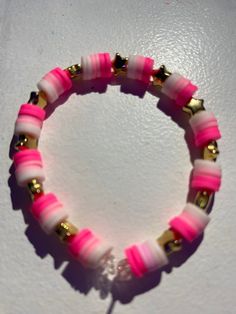 a pink and white bracelet with gold accents on the end is sitting on a table