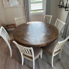 a wooden table with white chairs around it in front of a window and gray curtains