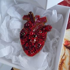 a red heart brooch sitting on top of a white box