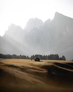 a lone house in the middle of a field with mountains in the background and foggy sky