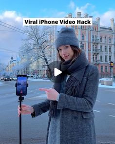 a woman standing next to a street holding a cell phone in her hand and pointing at the camera