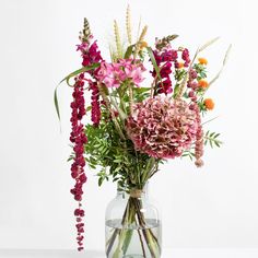 a glass vase filled with lots of flowers on top of a table next to a white wall