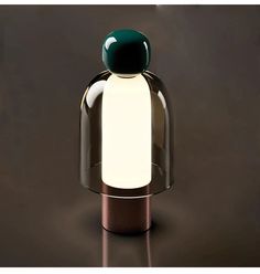 a glass and metal table lamp with a green light on it's top, against a dark background