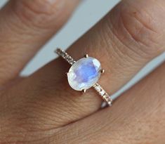 a woman's hand wearing a ring with an oval shaped rainbow colored stone on it