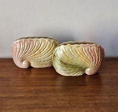 two ceramic vases sitting on top of a wooden table next to a white wall