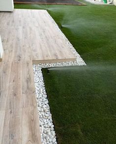 a wooden walkway with white rocks and grass on the ground next to a building that has a green lawn