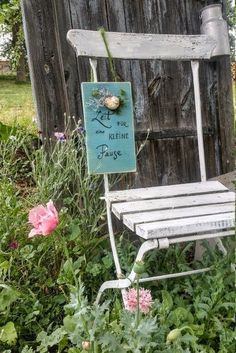 a white chair sitting in the middle of a garden next to a wooden fence and pink flowers