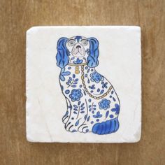 a ceramic tile with a dog painted on it's face and blue flowers around its neck