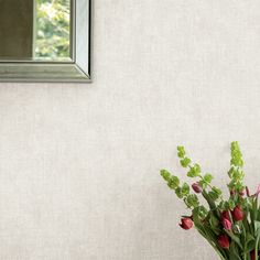 a vase filled with red flowers next to a mirror on a white wallpapered wall