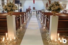 an aisle lined with flowers and candles in front of pews at the end of a church