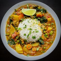 a white bowl filled with rice and vegetables on top of a wooden table next to a slice of lime