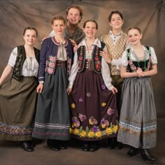 a group of people standing next to each other in front of a wall wearing dresses