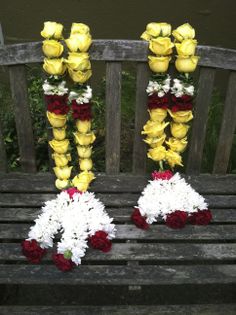 two yellow and red flowers are sitting on a park bench next to some white and red flowers