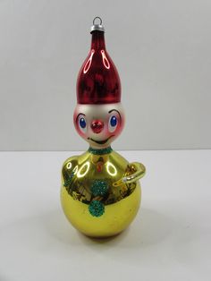 a glass ornament with a red hat on it's head sitting in a gold bowl