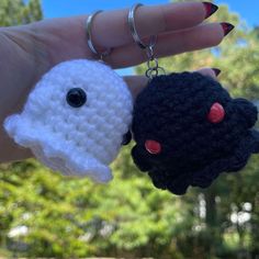 two crocheted keychains with black and white faces on them, one being held by a woman's hand