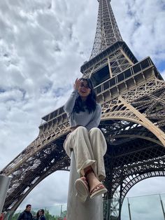 a woman sitting on top of a statue in front of the eiffel tower