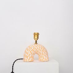 an orange and white table lamp with a black cord around it's base on a white surface