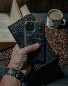 a person holding an iphone case in their hand next to a book and coffee cup