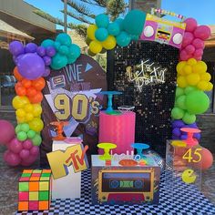 a table topped with lots of balloons next to a party sign and radio on top of a checkered table cloth