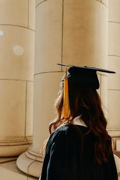 a woman wearing a graduation cap and gown standing in front of pillars with columns behind her