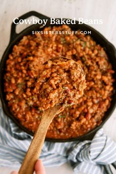 a hand holding a wooden spoon full of baked beans in a skillet with text overlay