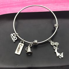 Every cheerleader loves to support her team and show spirit.  This adorable cheer themed charm bangle bracelet is adorned with:  - cheerleader  - megaphone  - word cheer  - go team  Silver in color, trendy styled stack-able charm bangles that's sure to be a hit. Expands to fit most wrists. Christmas gift for her, stocking stuffer or team gifts throughout the year.  Expandable style bangle is made if stainless steel.  Adult 60mm in diameter Tween 55mm in diameter for smaller wrists and young girl Cheerleader Jewelry, Short Quote, Cheerleading Gifts, Charm Bangles, Go Team, Organza Pouch, Engraved Pendant, Christmas Gift For Her, Bangle Bracelets With Charms