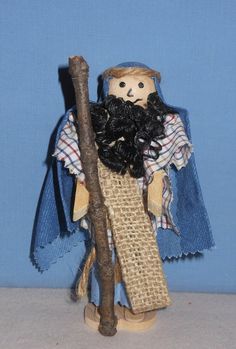 a wooden doll holding a stick and wearing a blue cape with black hair on it's head