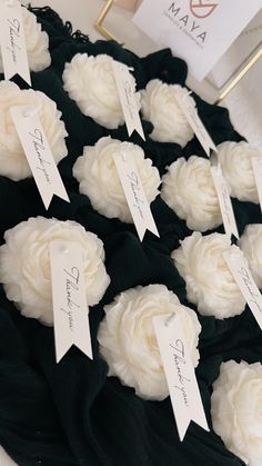 cupcakes with white frosting and name tags are on a black table cloth