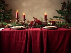 the table is set for christmas dinner with red linens and pine cones on it