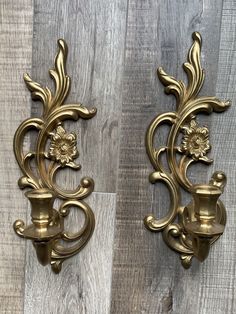 two gold wall sconces with flowers on them against a wood flooring background