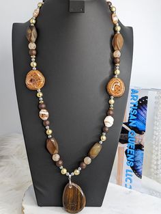 Here is another statement necklace from our collection! It is comprised of brown and tan beads ranging from wood, mosaic glass, tiger's eye, gold toned acrylic, brown quartz, and silver acrylic beads. The pendant is tiger's eye and it was delicately sourced by a member of the Artisan Queens. The clasp is a lobster claw and it's tough enough to withstand this 9 ounce stunner. Check out the rest of our collection for more present and future statement pieces! Happy shopping! Luxury Brown Beaded Necklaces In Elegant Style, Brown Polished Beads For Jewelry Making, Spiritual Brown Beaded Chain Necklaces, Artisan Brown Beaded Chain Beads, Brown Polished Beads Long Necklace, Unique Brown Jewelry With Polished Beads, Artisan Brown Beaded Chain, Unique Brown Polished Beads, Nature-inspired Brown Jewelry With Gemstone Beads