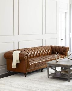 a brown leather couch sitting in a living room next to a coffee table and white walls