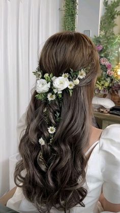 a woman with long hair and flowers in her hair is looking at the mirror while wearing a white dress