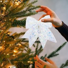 two hands are decorating a christmas tree with white paper and glitters on it