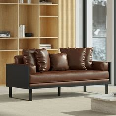 a brown leather couch sitting in front of a wooden book shelf next to a window