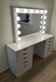 a white vanity with lights on it in a room next to a wall and hardwood floor