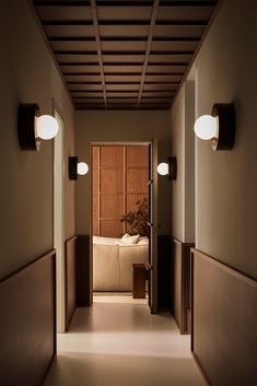 an empty hallway leading to a bedroom with a bed in the corner and two lights on either side