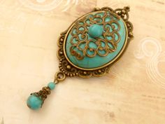 This large, unique brooch is a beautiful accessory that can be worn in many ways: on blouses, sweaters, vests, jackets, scarves, cases, hats, backpacks, bags, bridal bouquets and much more. The brooch consists of a solidly crafted jewelry setting made of bronze-colored metal and a large turquoise cabochon, which is also decorated with an ornate metal ornament and another small turquoise cabochon. A jewelry pendant with turquoise beads is attached to the bottom of the brooch. The brooch, including the pearl pendant, measures 8.3 L x 3.5 W cm. A MATCHING HAIR CLIP YOU WILL FIND IN MY SHOP- Gemstone Brooch, Unique Brooch, Metal Ornament, Bridal Bouquets, Crafted Jewelry, Jewelry Pendant, Turquoise Beads, Bronze Color, Pearl Pendant