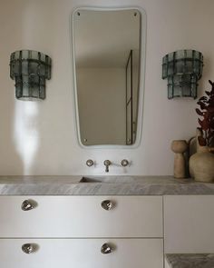 a bathroom with a sink, mirror and two vases