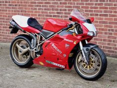 a red motorcycle parked next to a brick wall