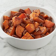 a white bowl filled with sweet potatoes and pecans on top of a marble counter