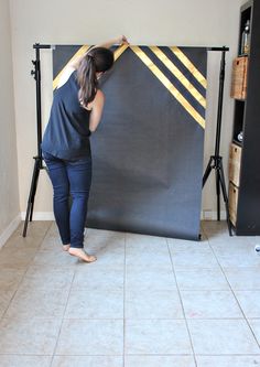 a woman standing in front of a black backdrop with gold lines on it and another person behind her