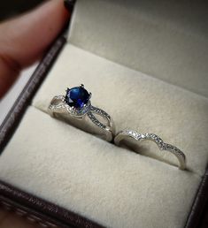 someone is holding their engagement ring in the box with it's blue stone and diamond accents